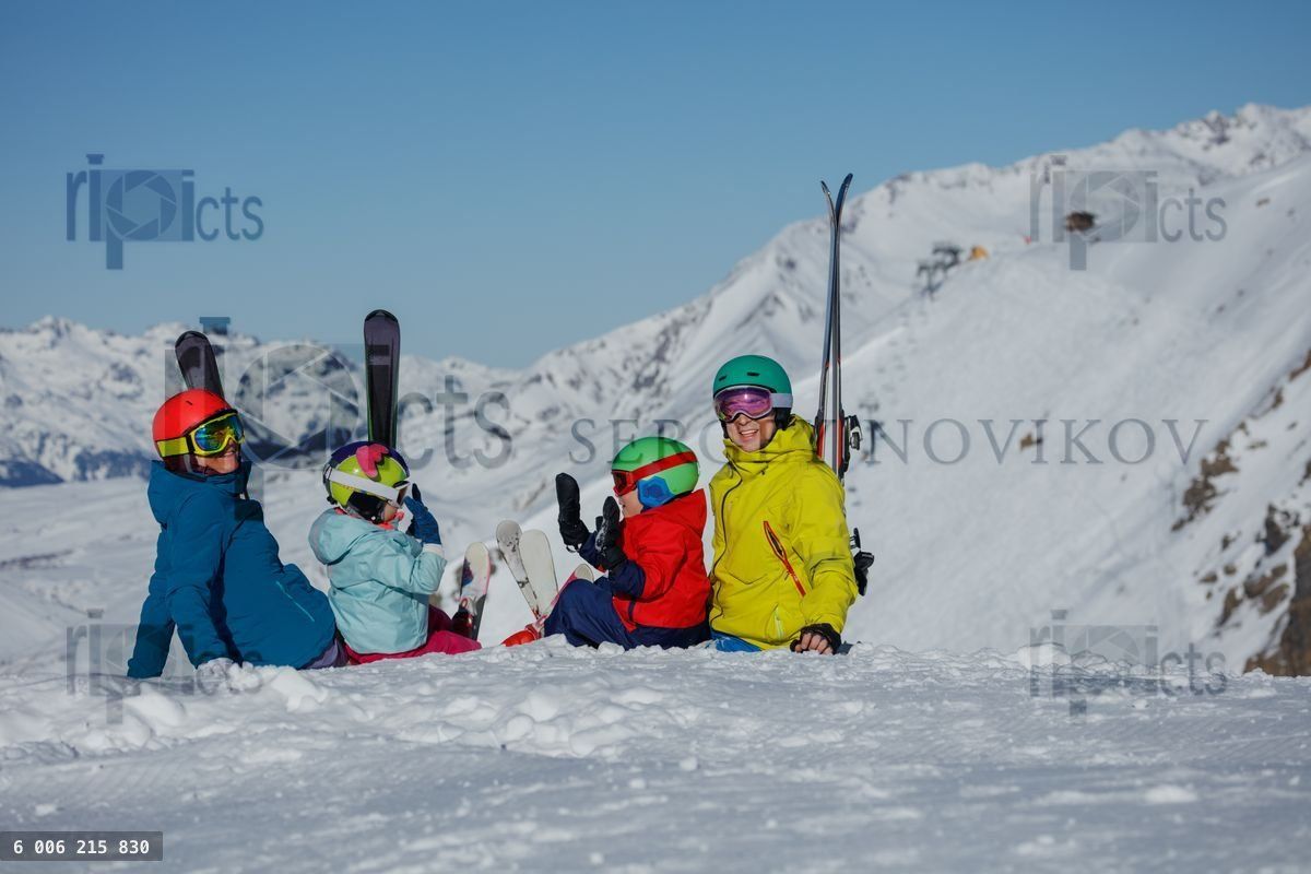 Four people, prepared for skiing, sit on a snow-covered slope