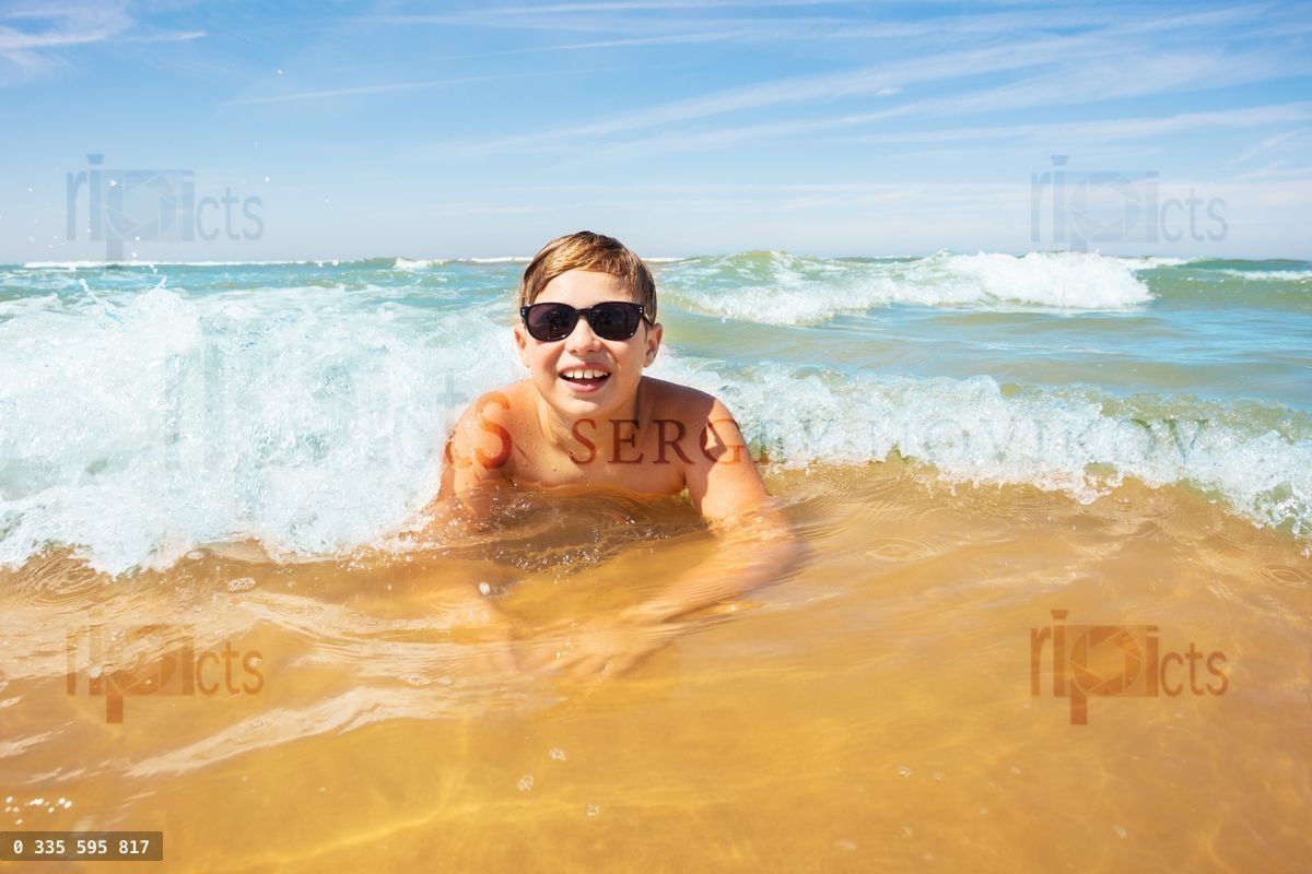 Boy have fun in sea waves laying on sand beach