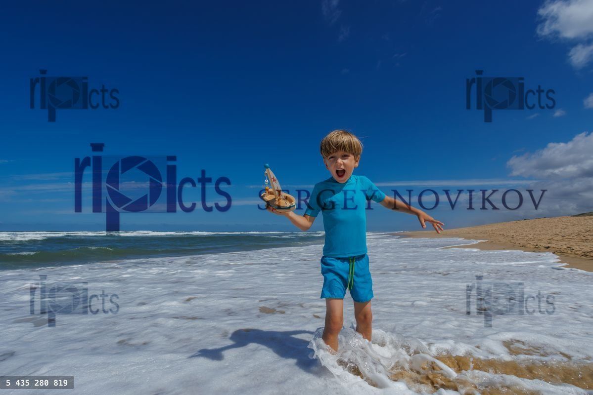 Young boy joyfully playing with a toy boat at the beach