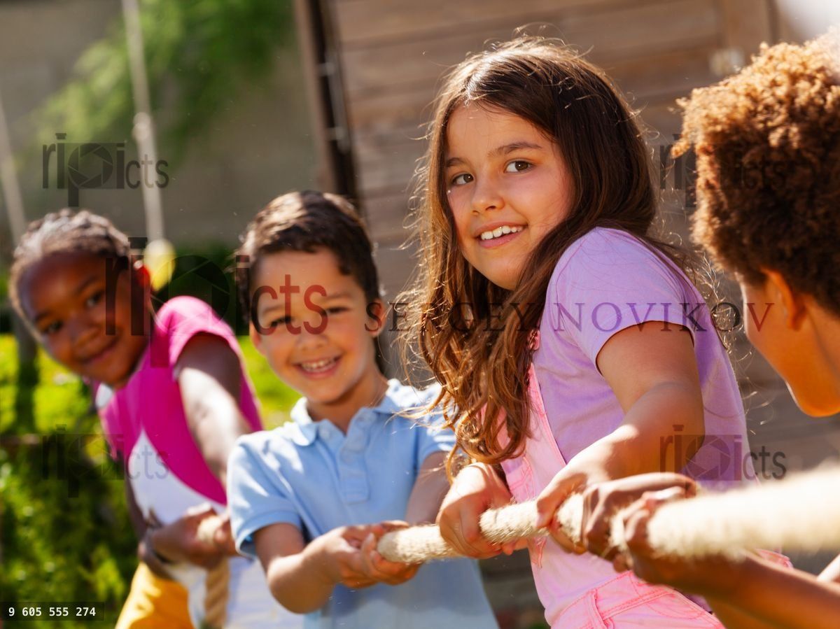 Girl in group of diverse kids pull rope play game