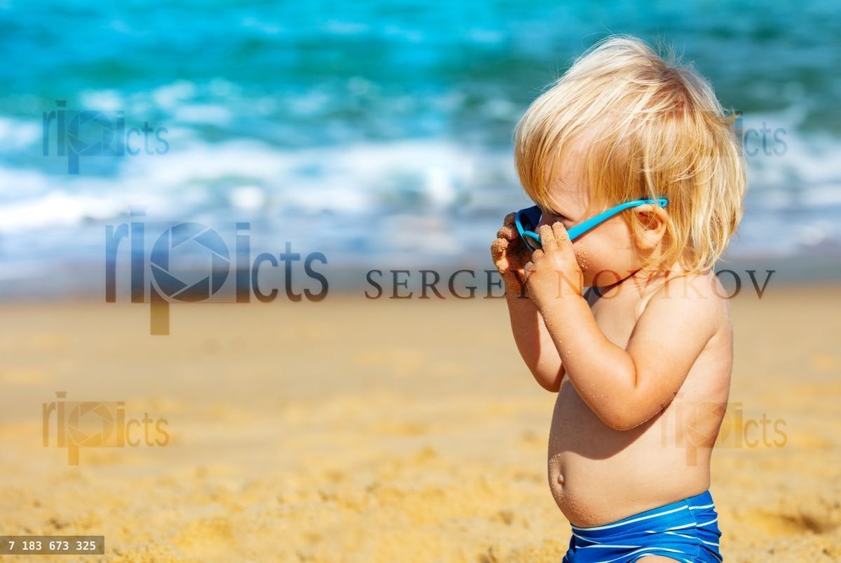 Wondering little boy with sunglasses on the beach