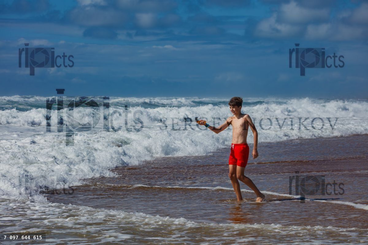 Young boy in red shorts playing at beach with waves on vacations