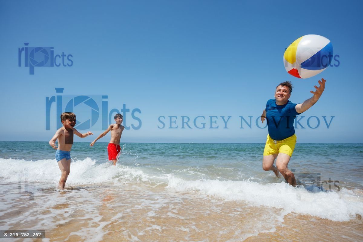 Boys throw beachball to dad, enjoying funny beach game together