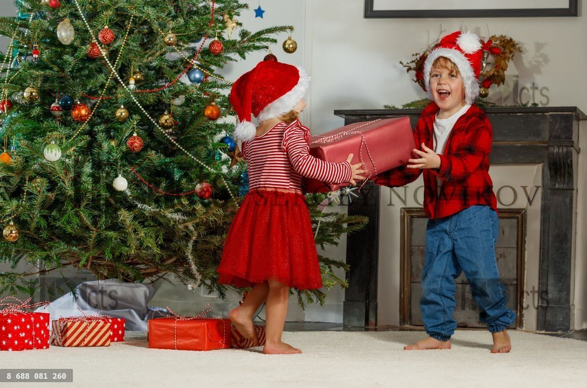 Enfants en bonnet de Père Noël partageant des cadeaux de Noël près d'un arbre décoré