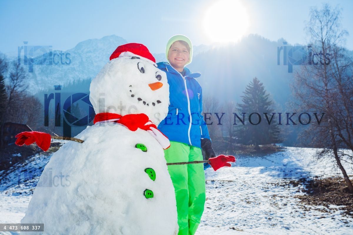 Happy boy in winter outfit stand with freshly build snowman