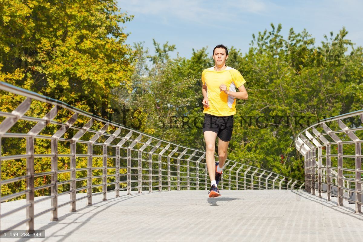 Young athletic man jogging on city bridge at park