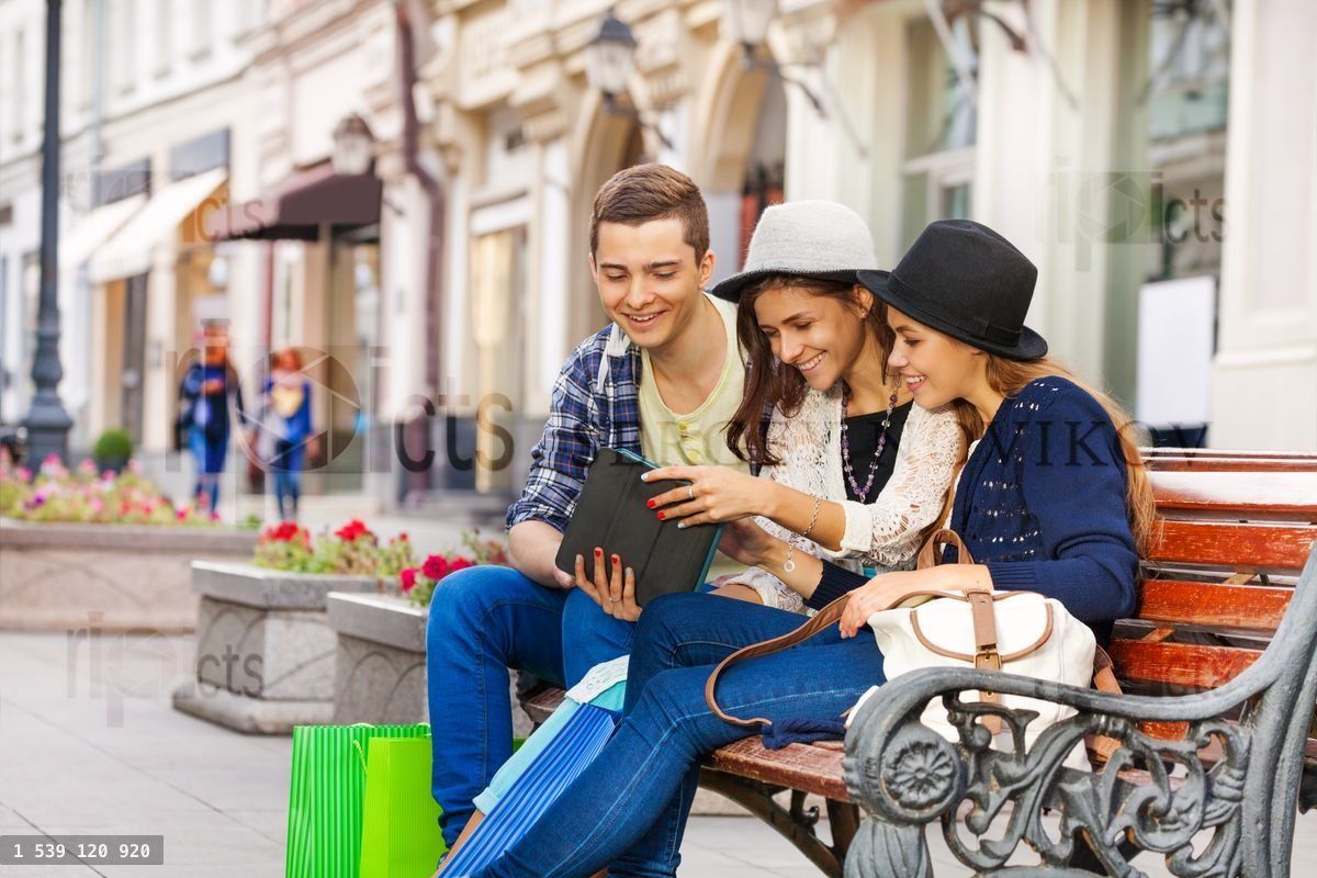Friends sitting together with tablet on the bench