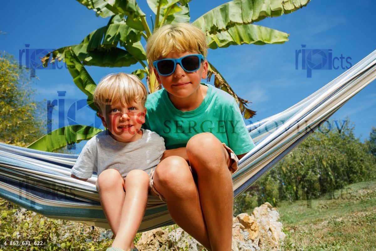 Boys sit in hammock at the garden over banana tree
