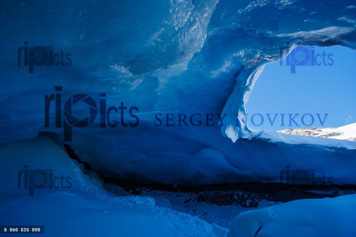 Blue ice cave with bright light seeping through ceiling opening