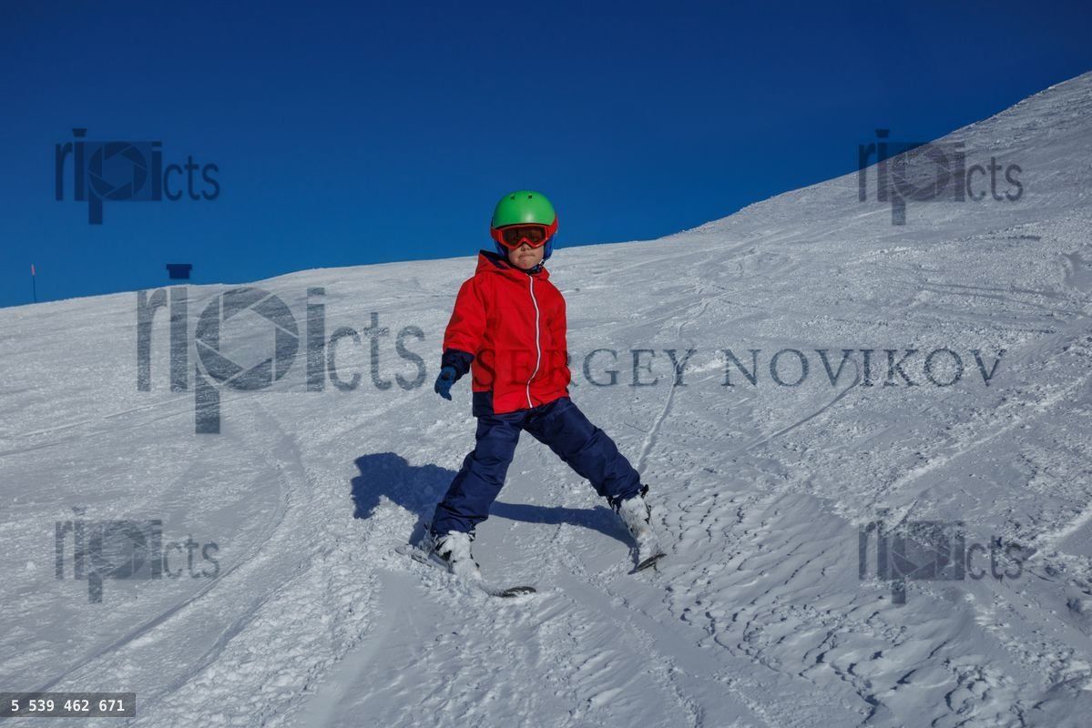 Young skier in red jacket practices wedge turns on a snowy slope