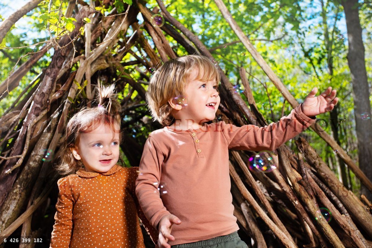 Deux enfants, un garçon et une fille, jouent avec des bulles de savon dans une hutte de branches