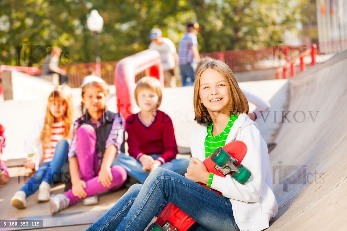 Girl sits in front with skateboard and other kids