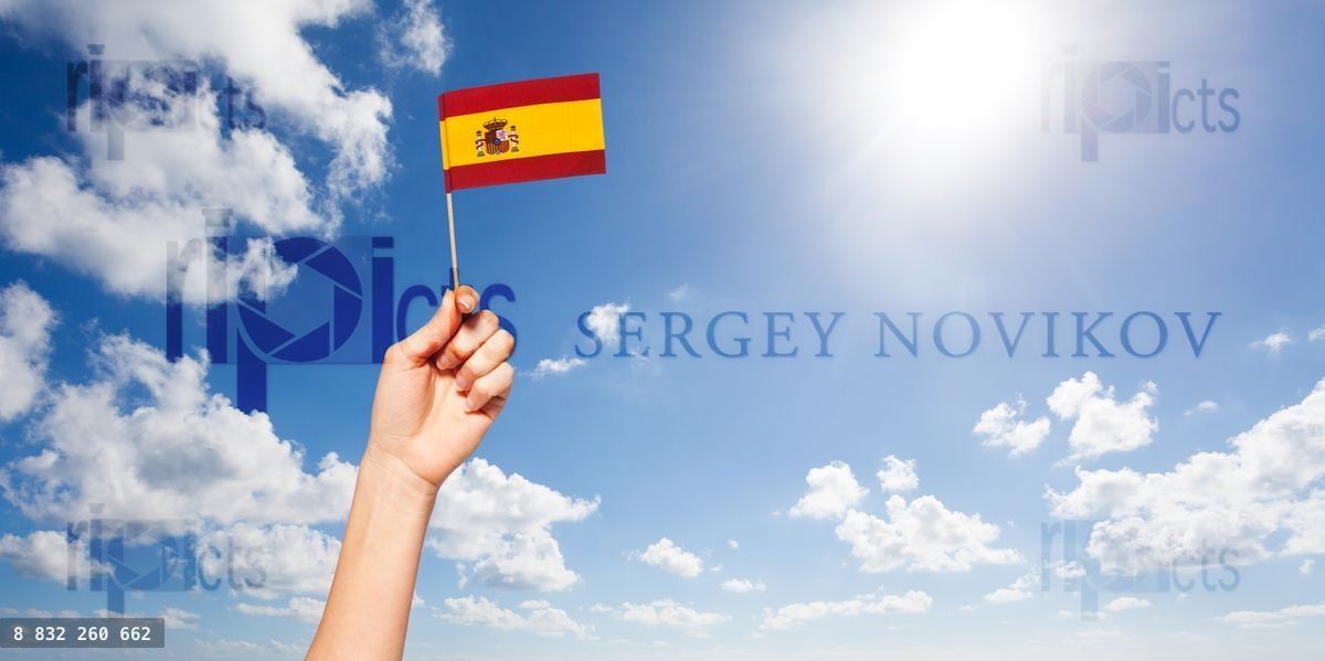 Woman's hand holding Spanish flag against blue sky