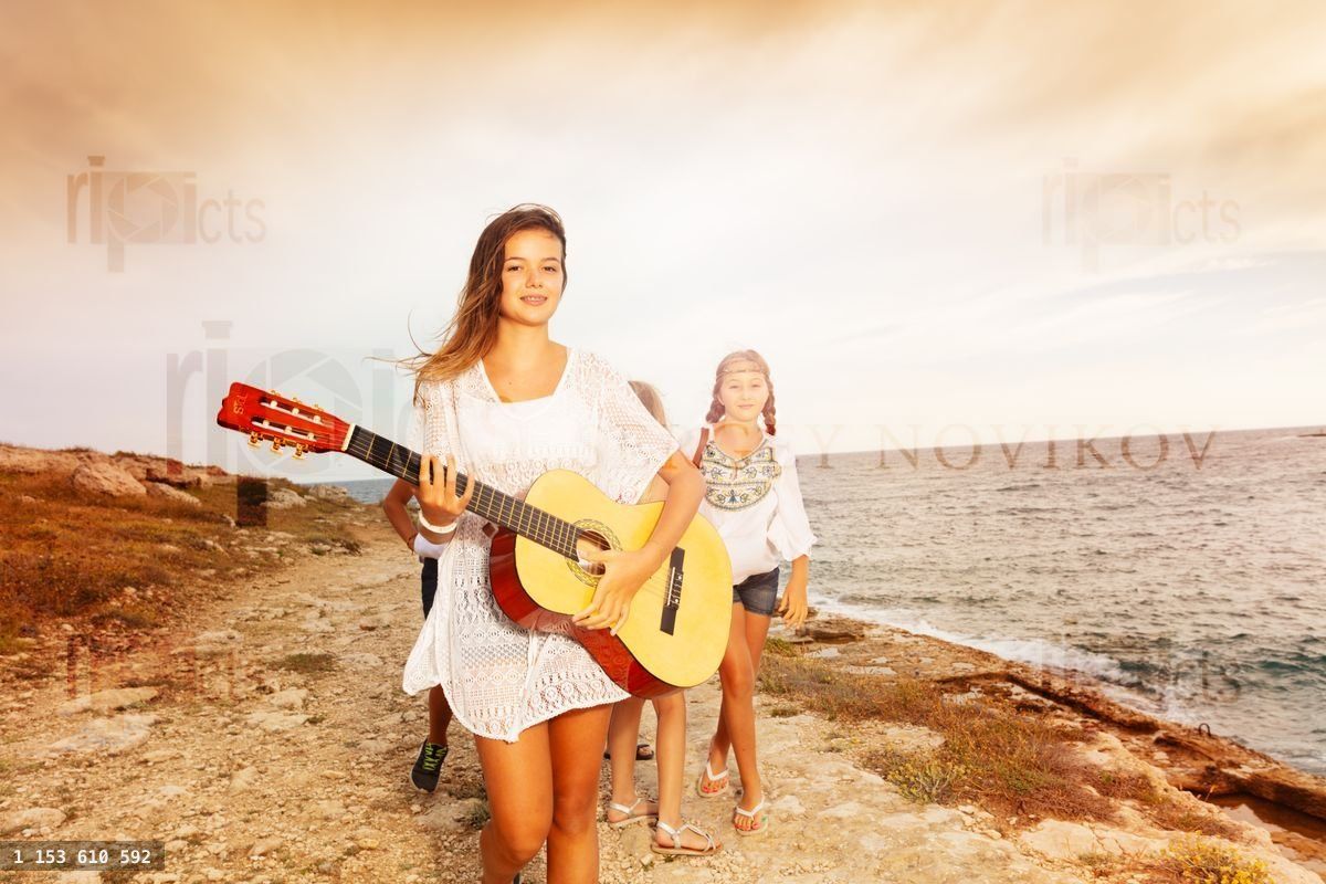 Young girl walking on the beach and playing guitar