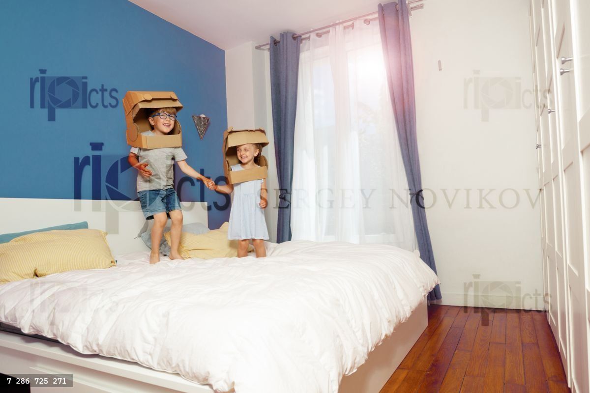 Boy and girl in cardboard space costumes jump on parents bed