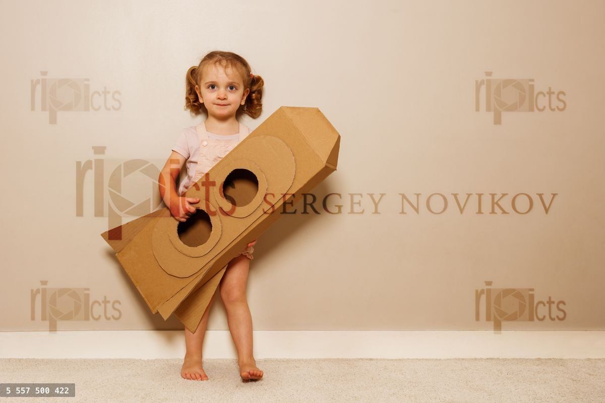 Young girl holds cardboard rocket, imagines space voyage