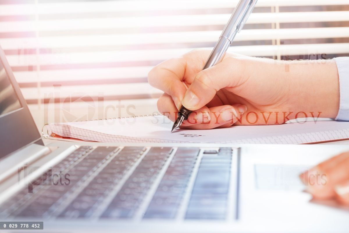 Hands using laptop and making notes on notepad