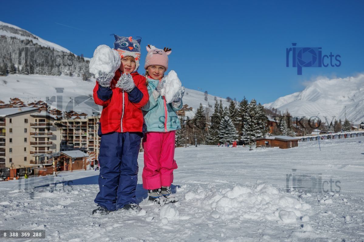 Two children display fresh snowballs proudly on a sunlit hilltop