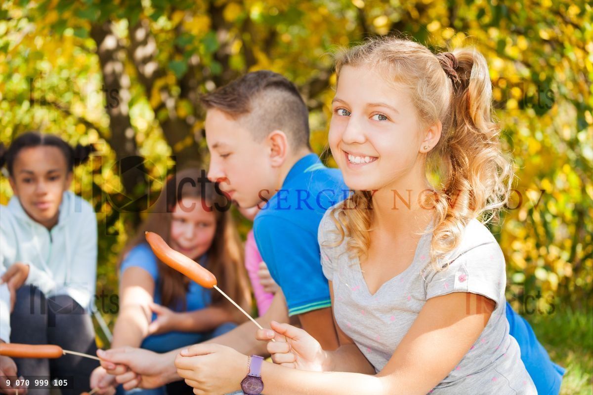Girl and teens sit on campsite with sausages