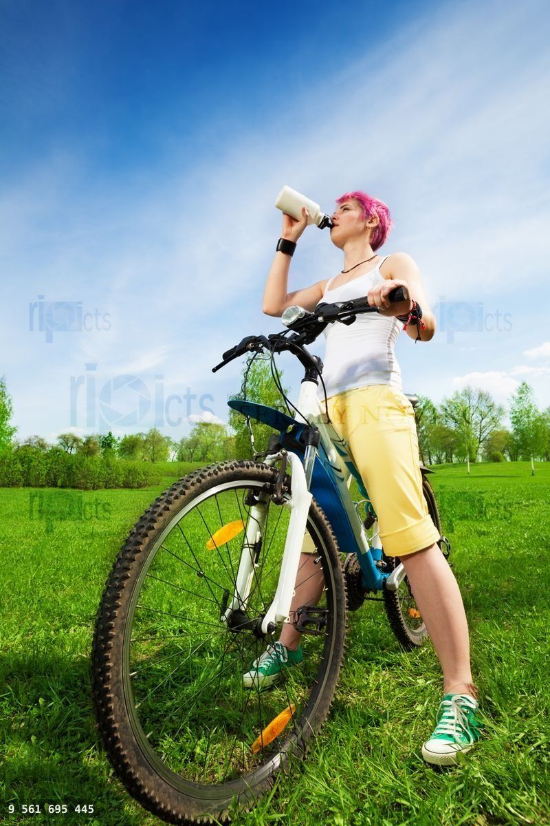 Young woman on a bike drinking water