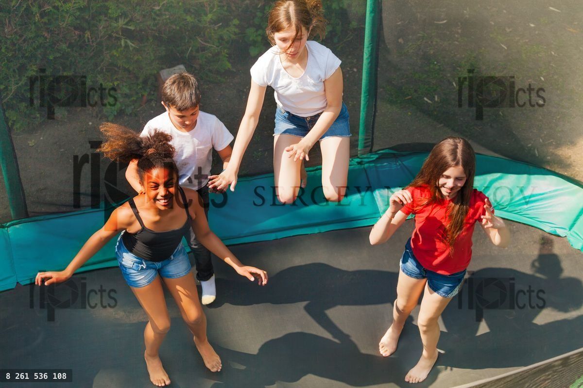 Four happy friends bouncing on outdoor trampoline