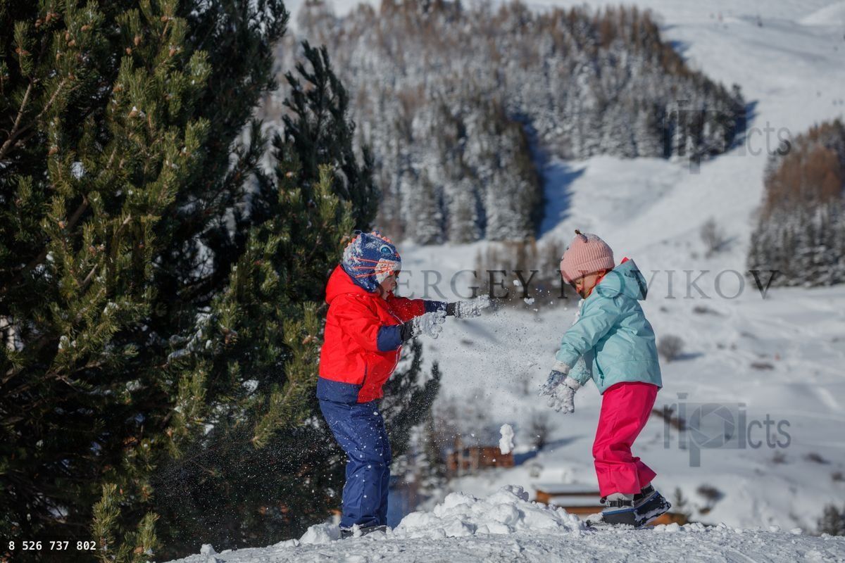 Two children toss snowballs at each other on a snowy hilltop