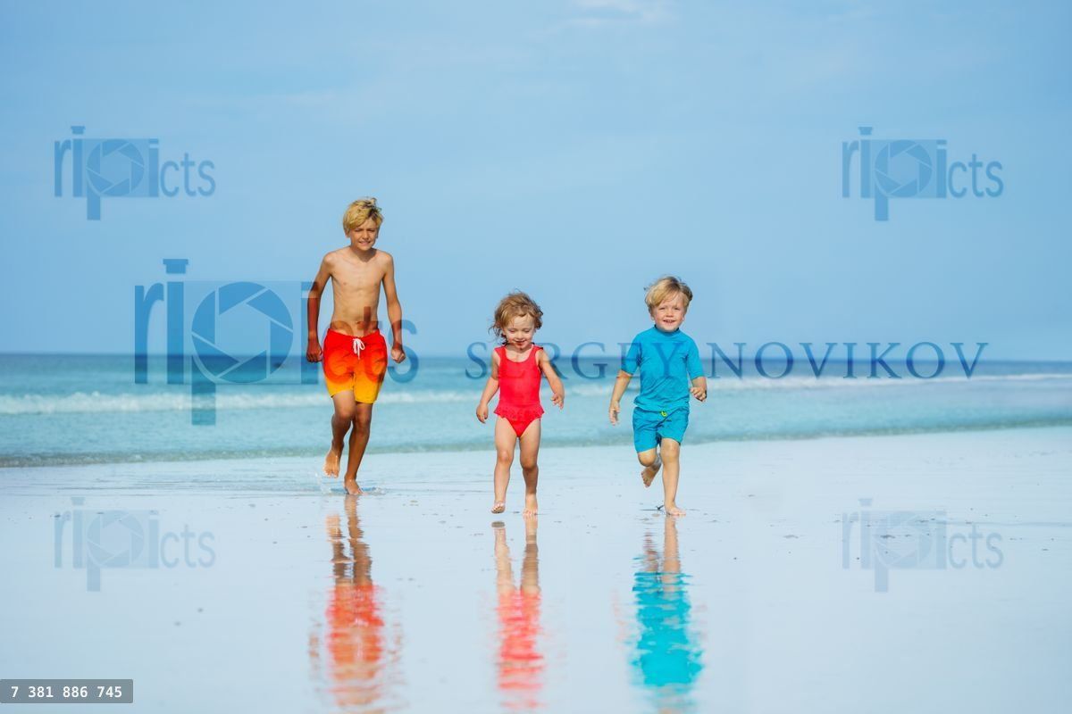 Trois enfants, garçons et fille, courent ensemble sur une plage de sable