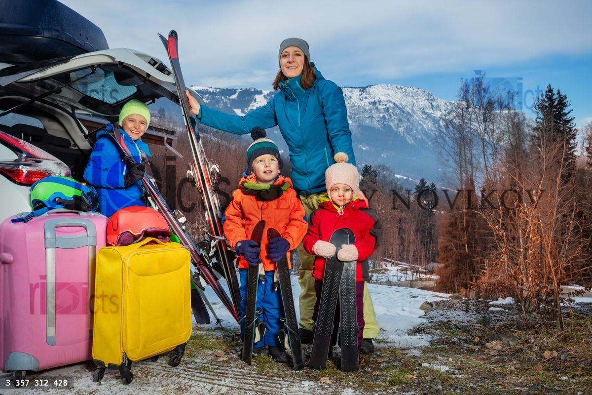 Mom at vacation stand holding ski by car arrived with 3 kids