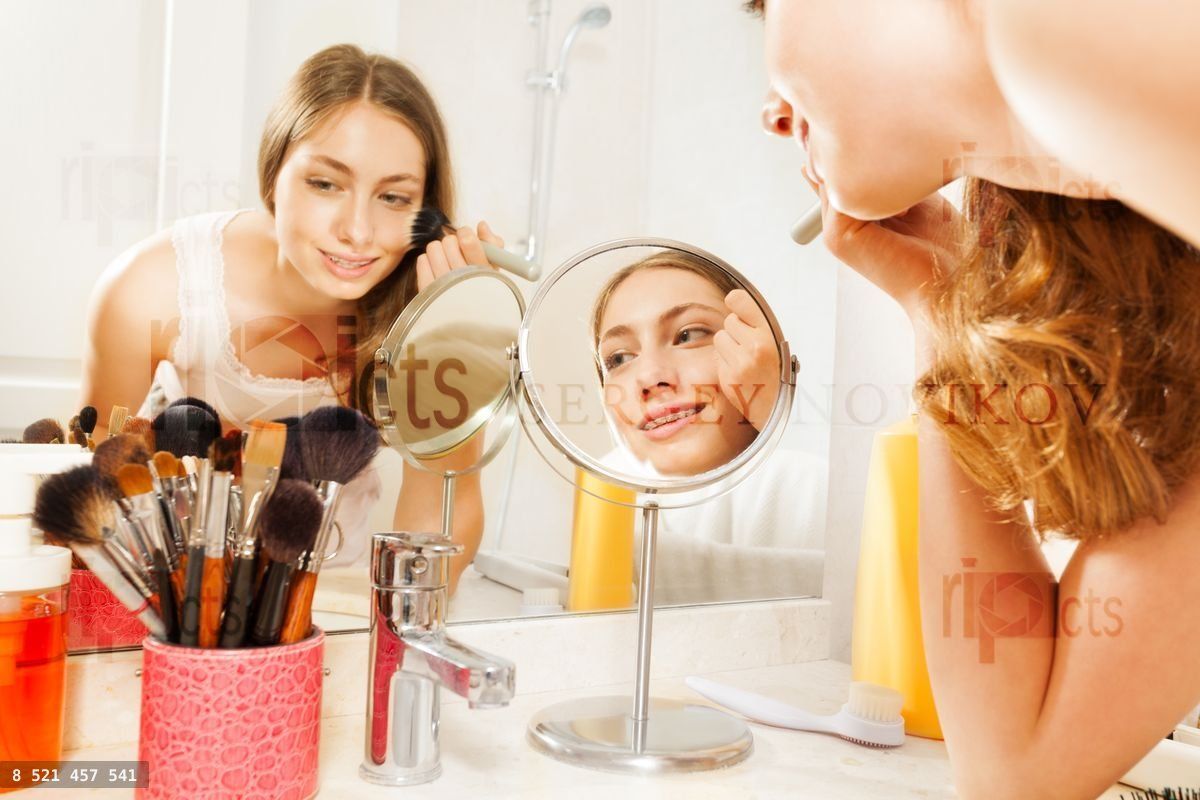 Young woman apply makeup, seen in bathroom mirror