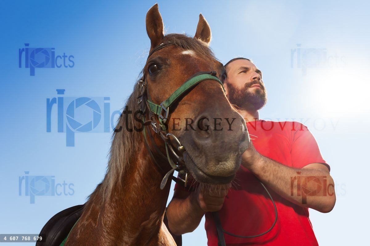 Young man with his bay horse against blue sky