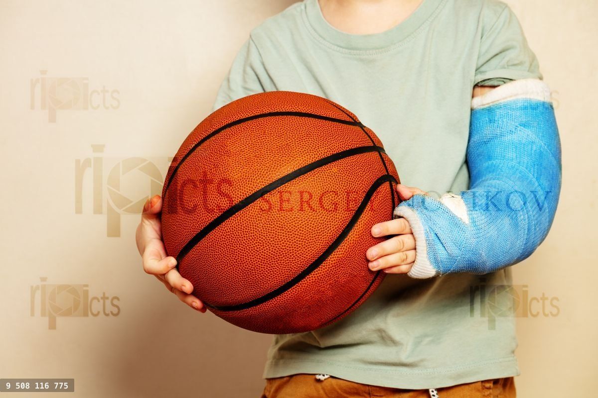 Big basketball ball in hands of boy with broken hand cast