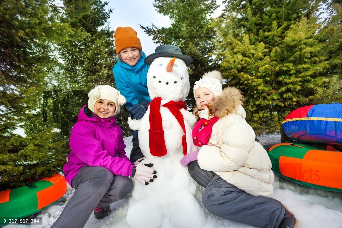 Three happy children sitting close to cute snowman