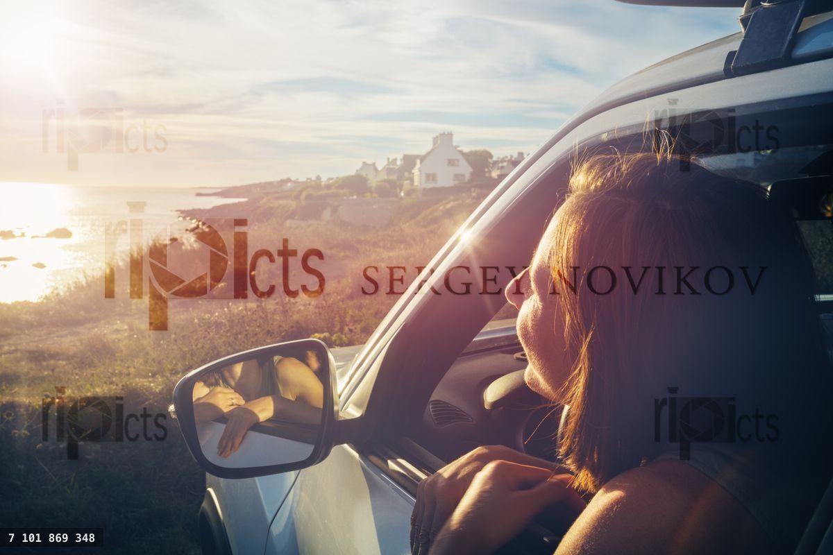 Woman on driver seat look at ocean sunset from car window