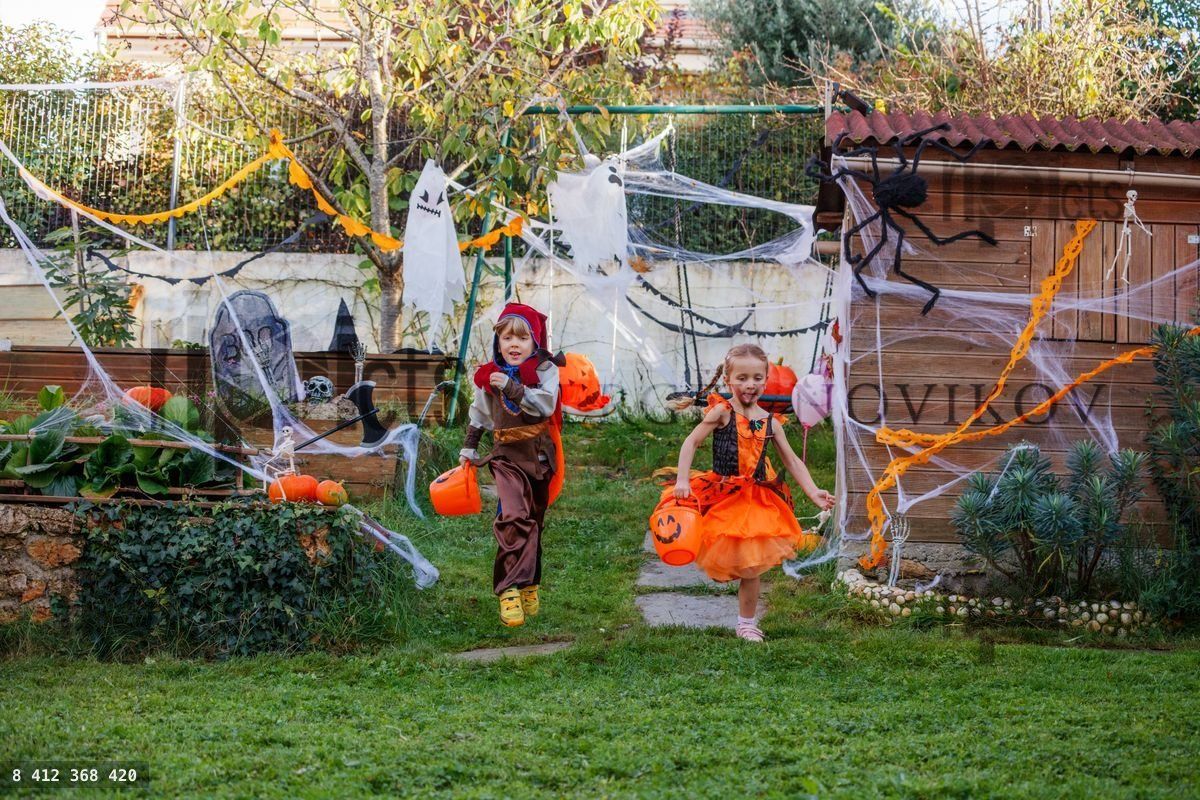 Three costumed kids sprint through Halloween yard with buckets