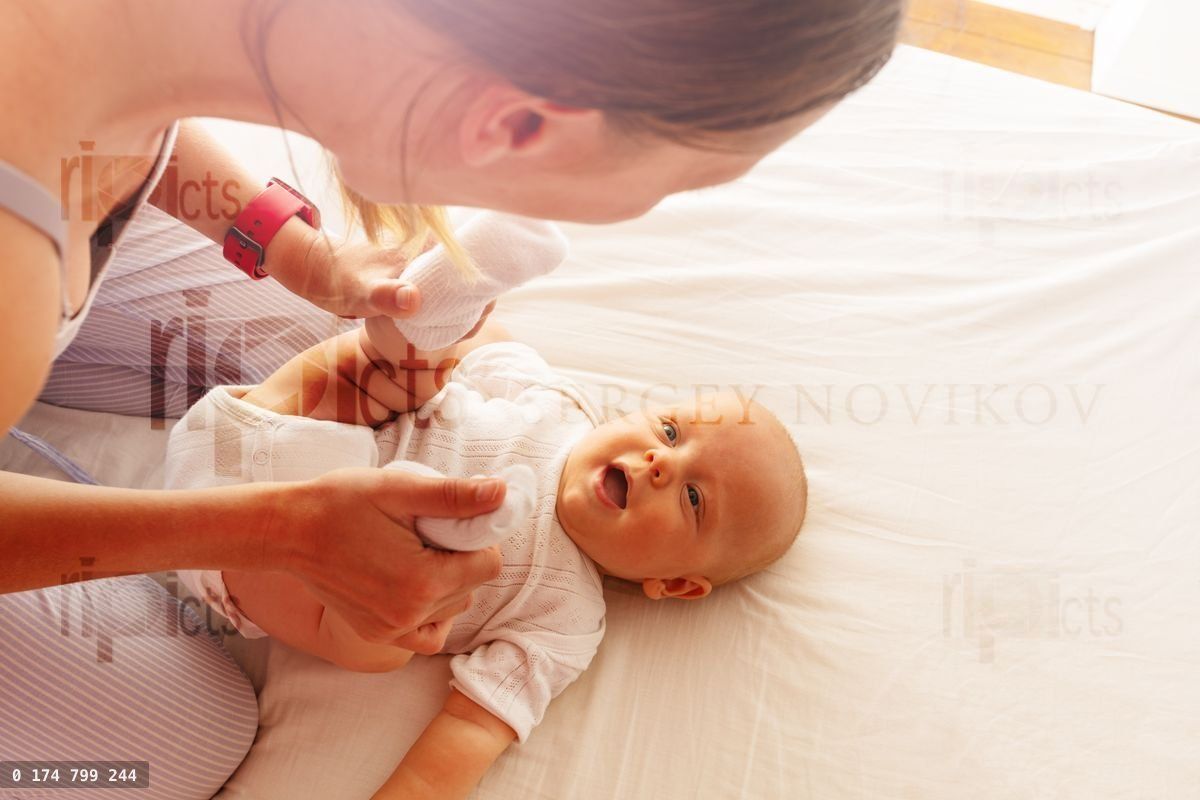 Young mother play with laughing infant on the bed