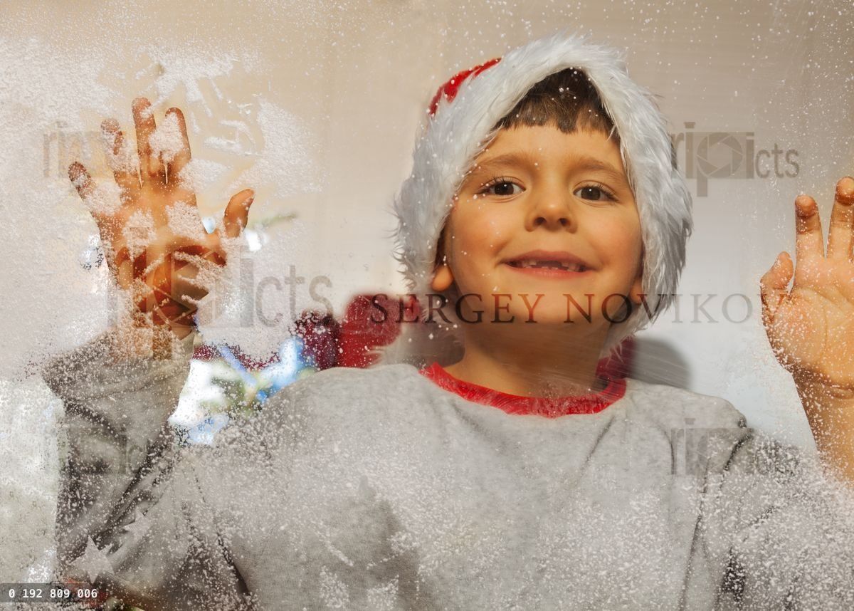 Boy in Christmas hat with decorated frozen window