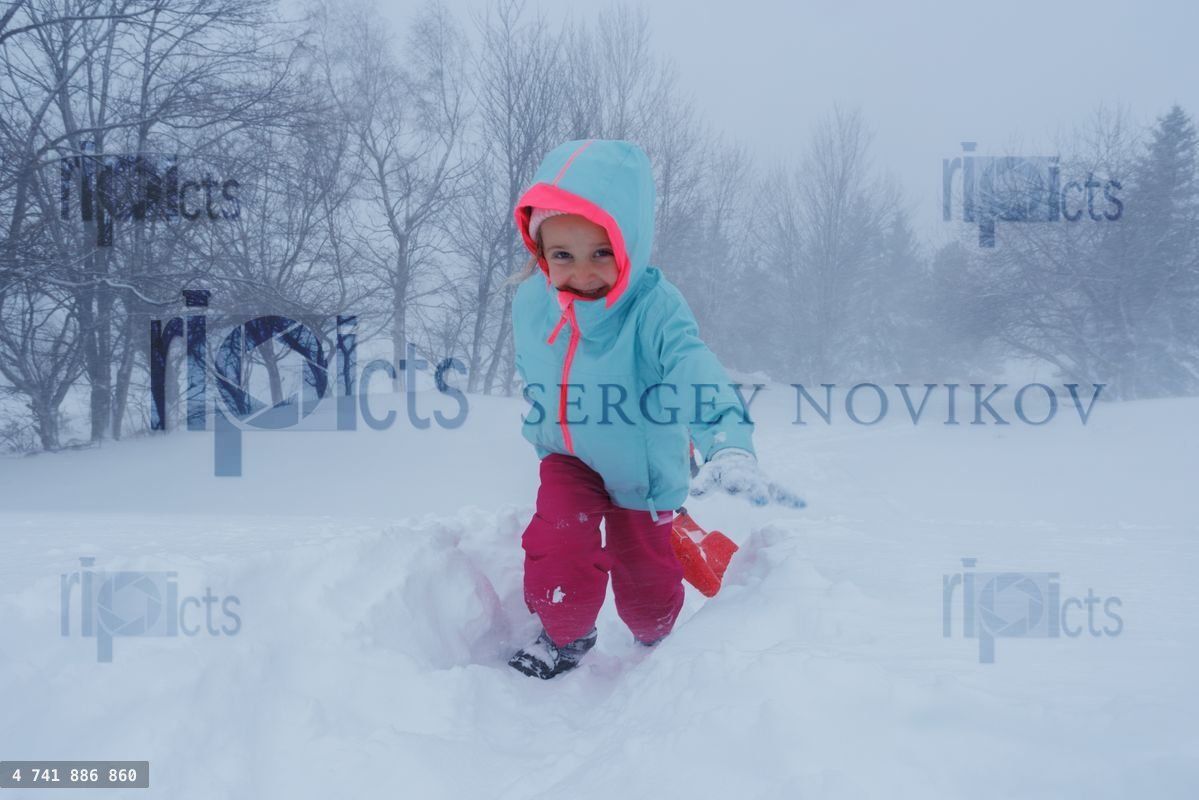 Young girl go through deep snow with bare trees in background