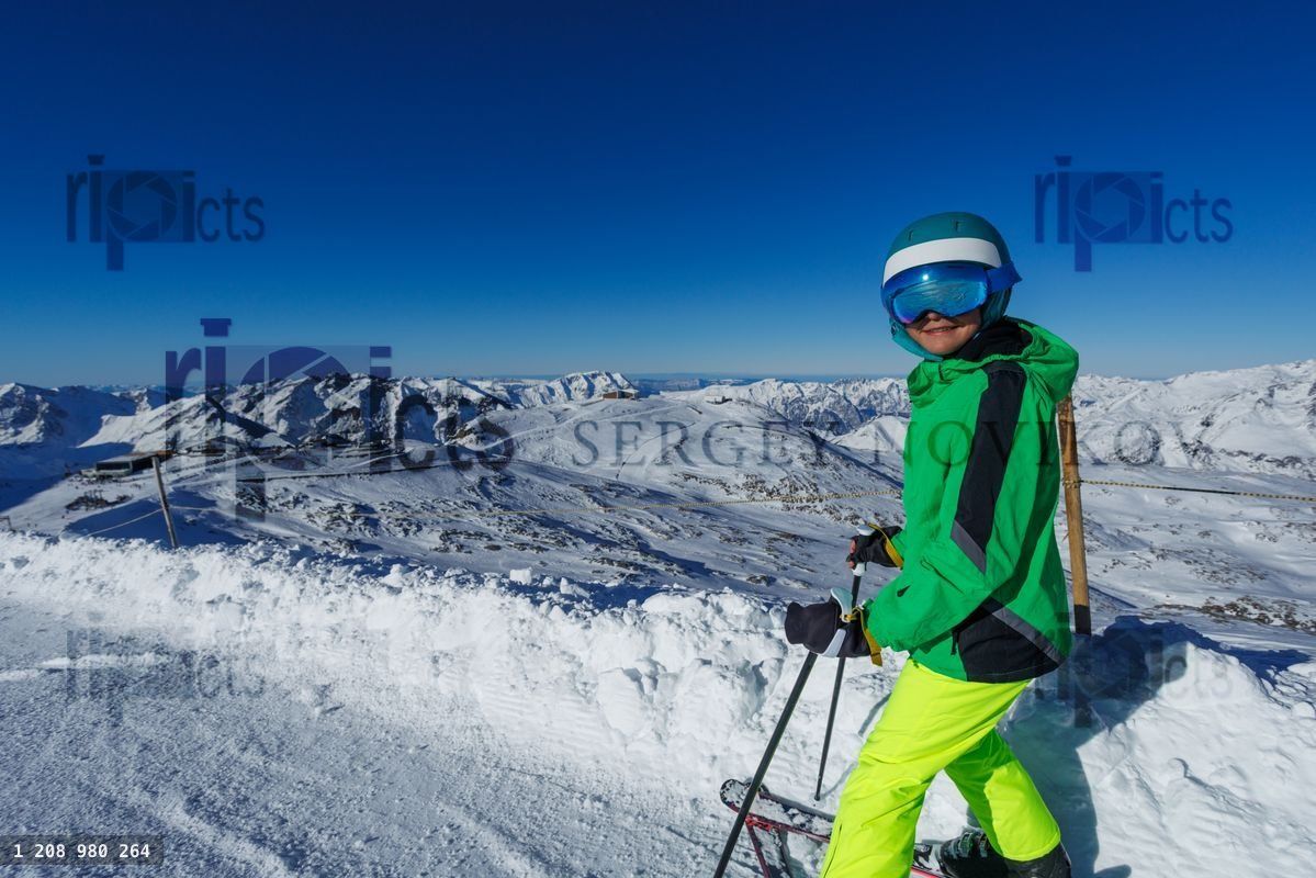 Happy boy skiing in colorful gear with snowy mountains around
