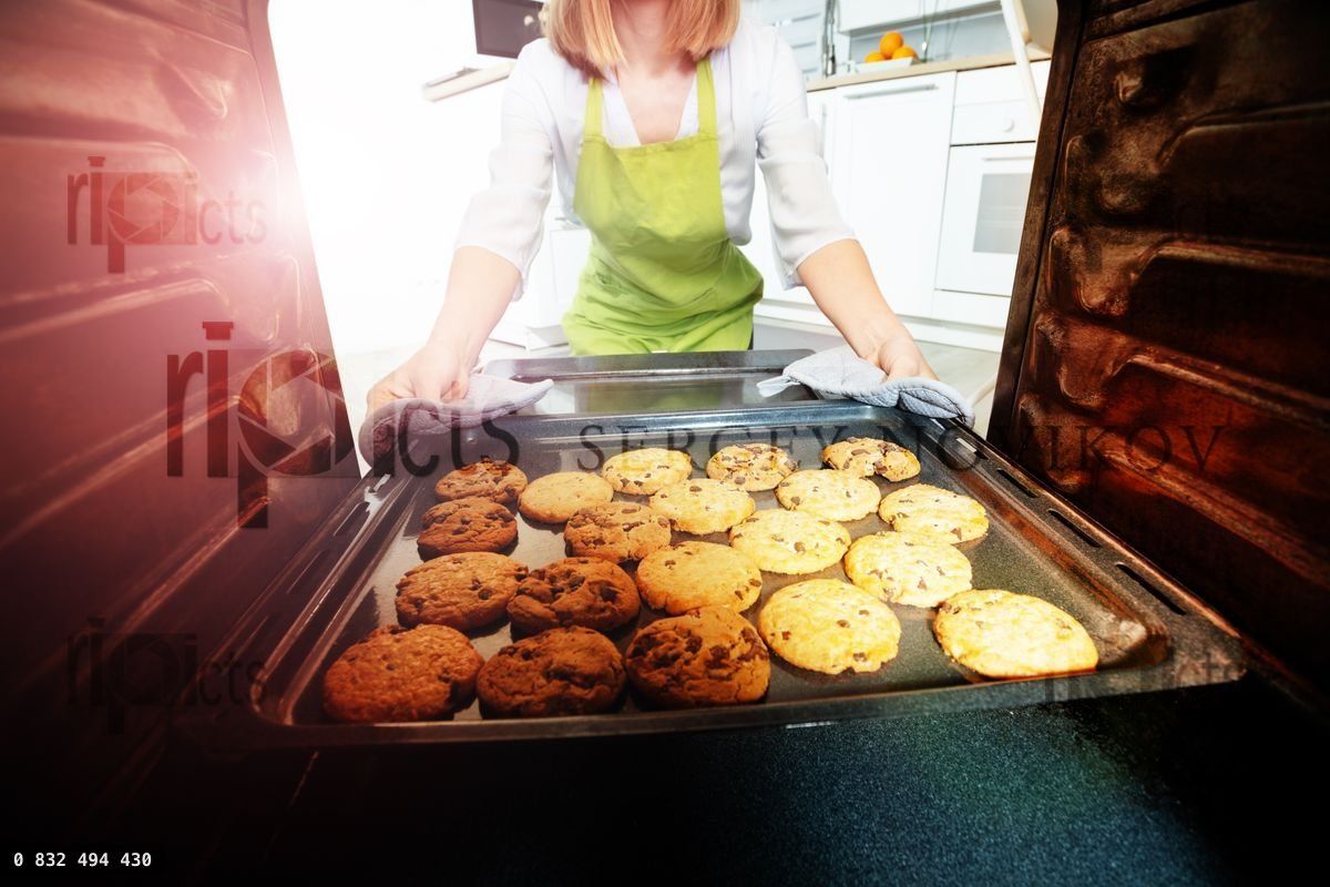 Young woman take freshly baked cookies from oven