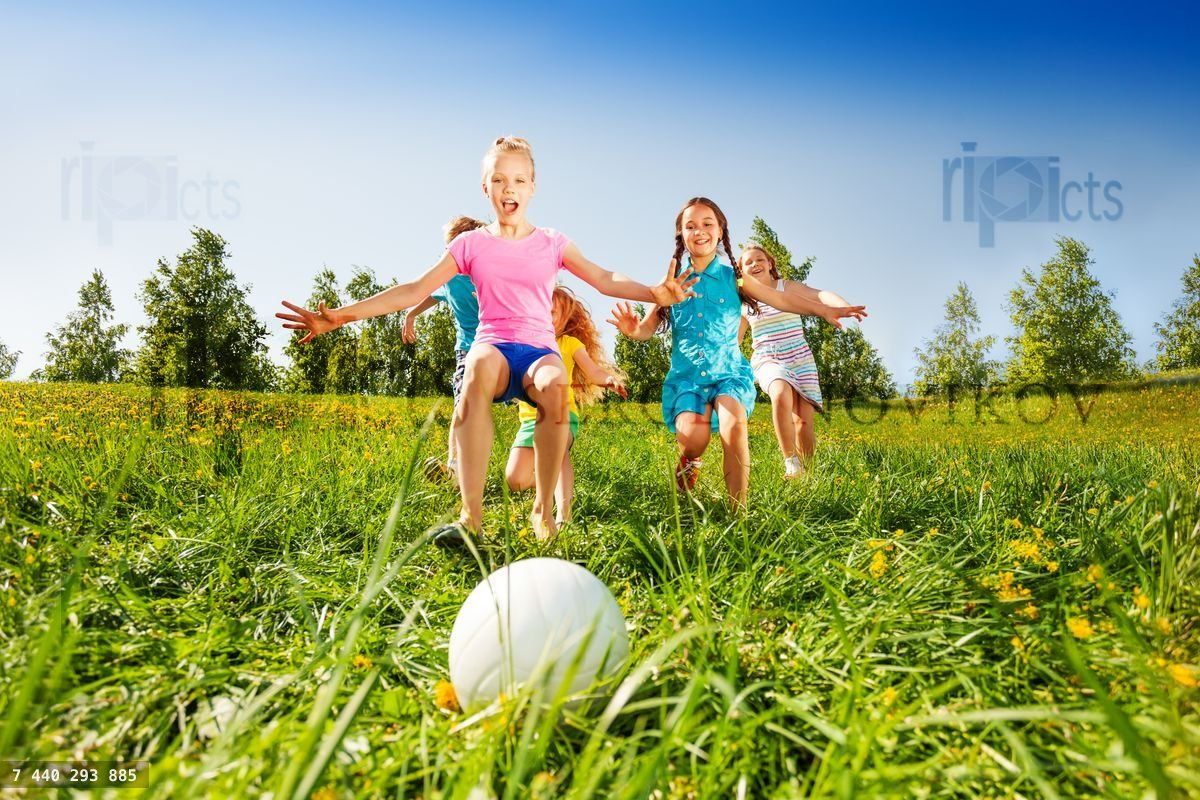 Group of kids running to the ball in meadow