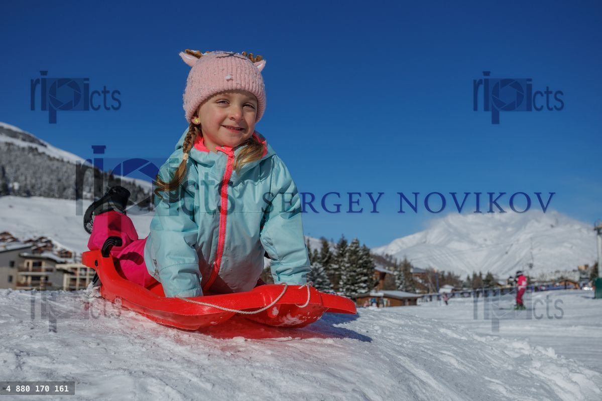 Young girl lay at sled enjoys sledding on a bright winter day