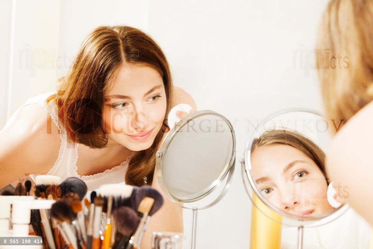 Woman cleaning face with cotton pad seen in mirror