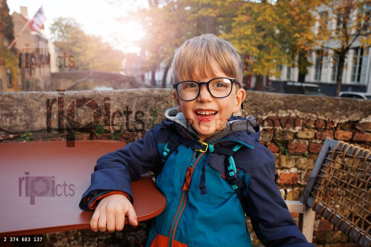 Young boy with glasses at outdoor table in autumn town setting