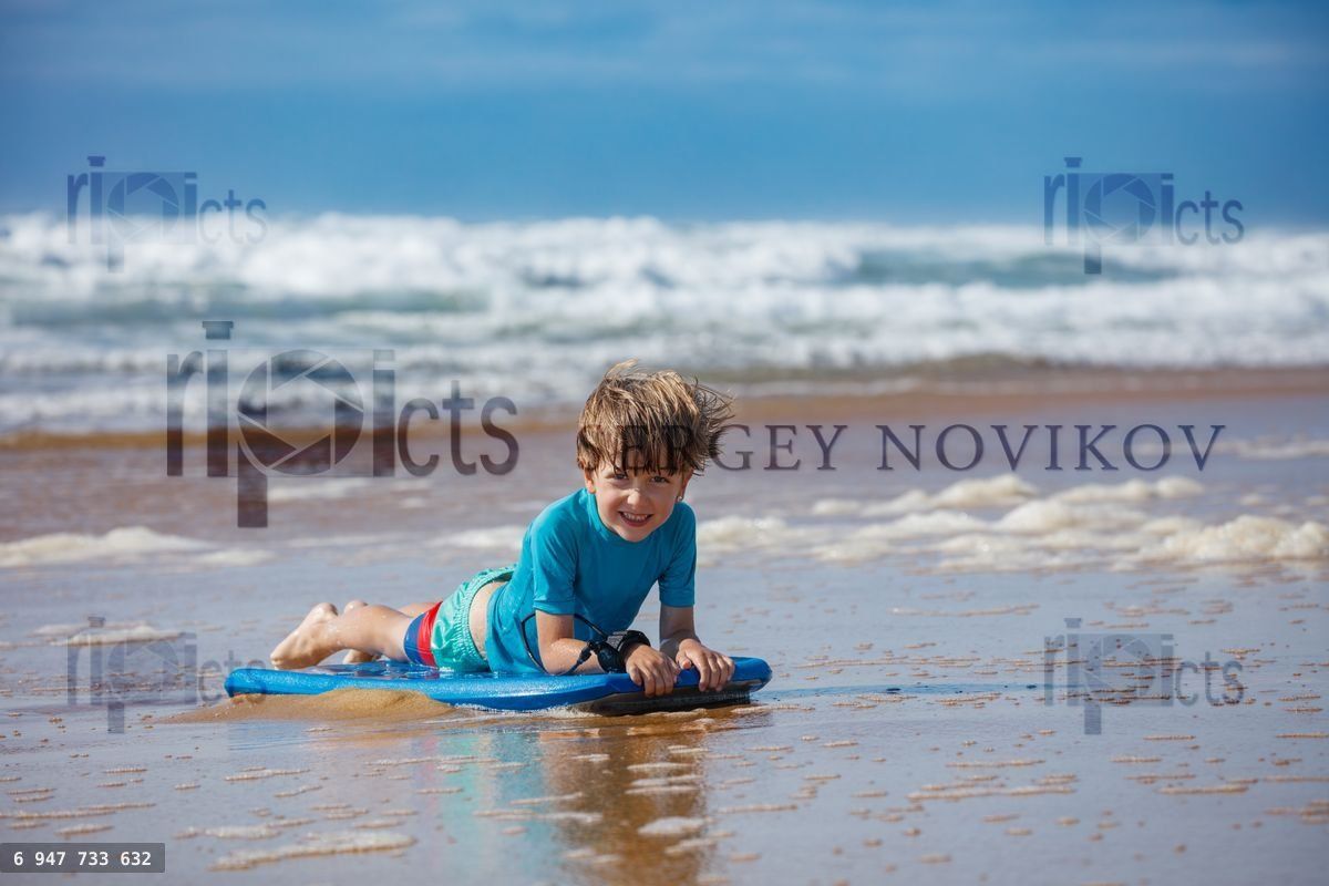 Young boy happily bodyboarding at sunny beach shore on vacation