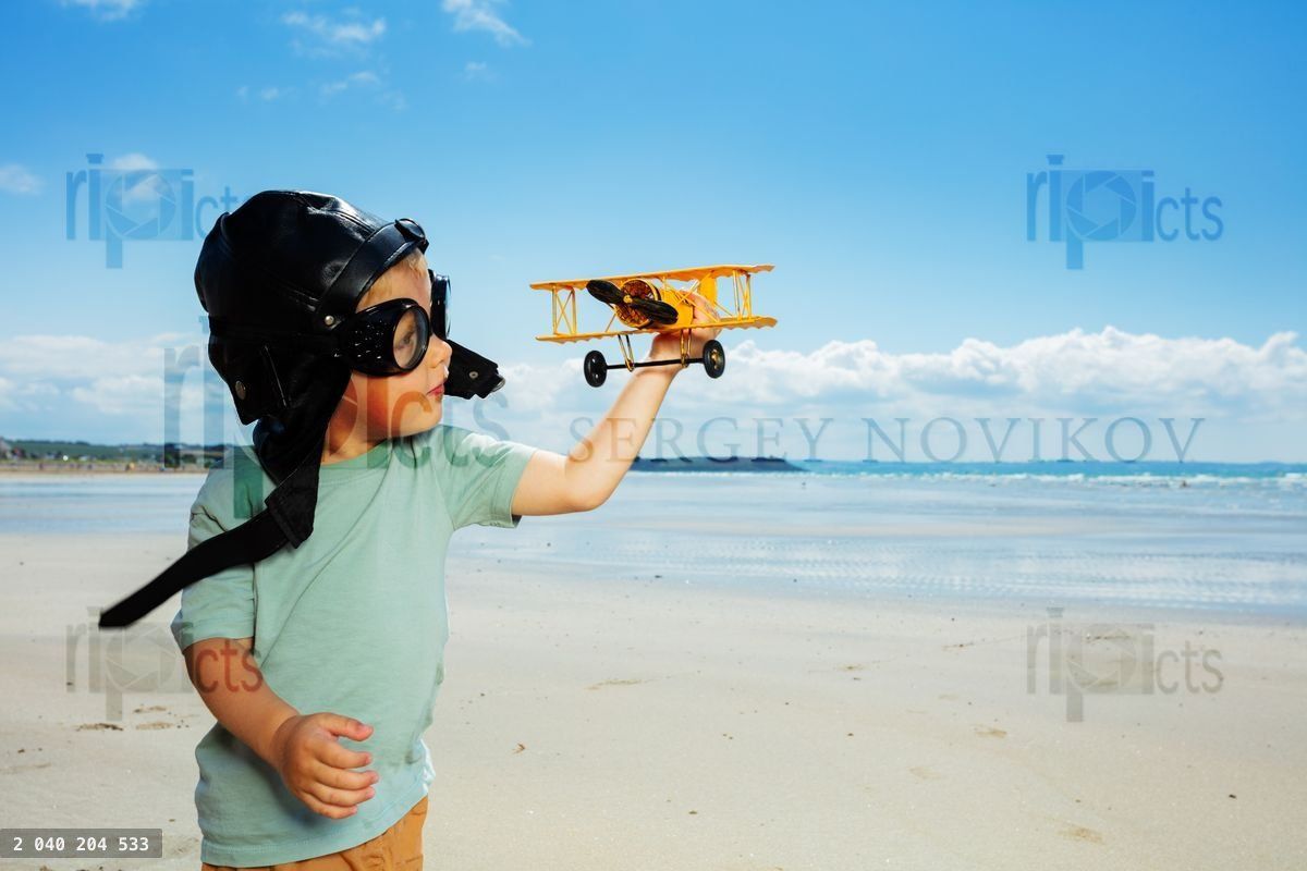 Boy in aviator hat and glasses play with toy plane