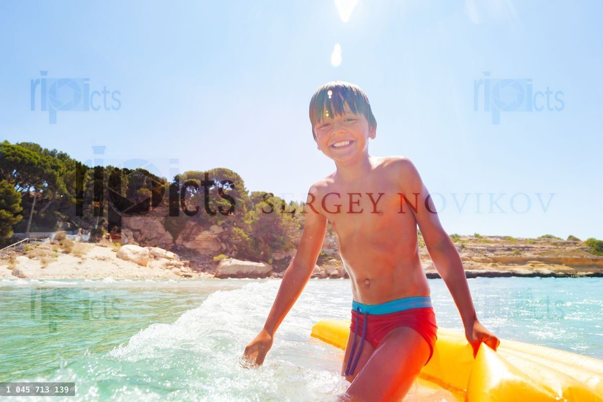Happy boy playing in waves with inflatable float
