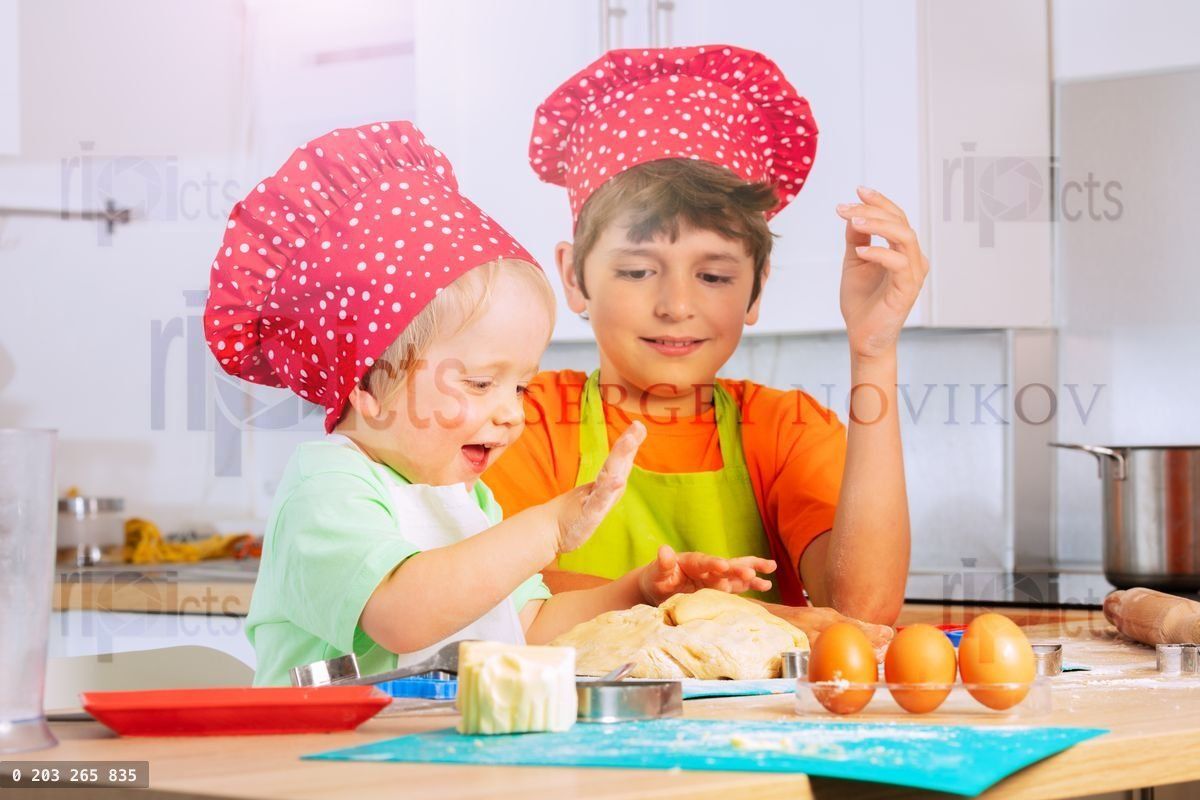 Two children crumble dough using hands at kitchen