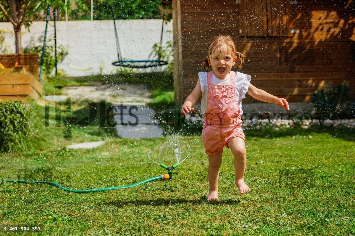 Fun in the garden beautiful girl run around water sprinkler