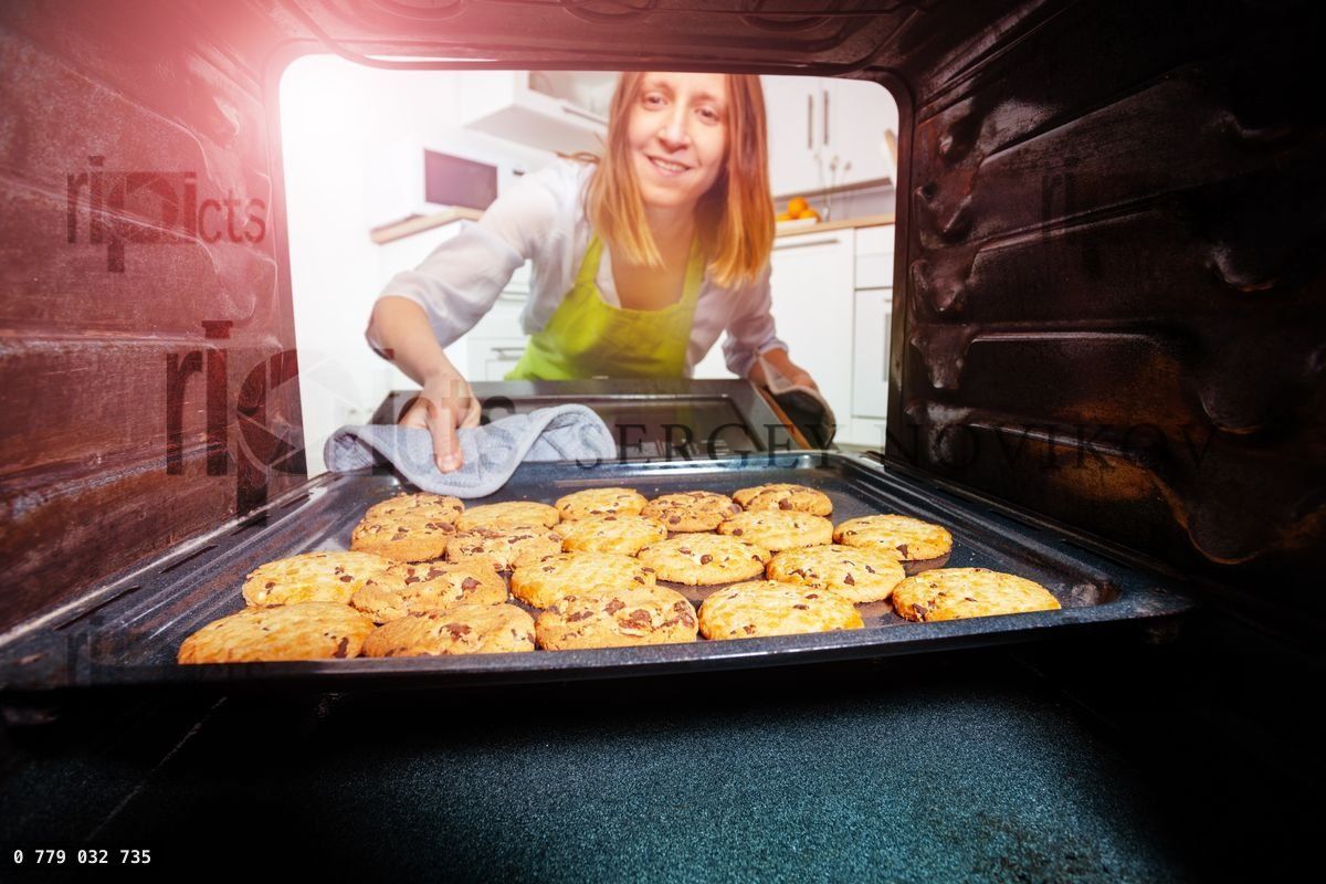 Woman taking fresh baked cookies tray from oven