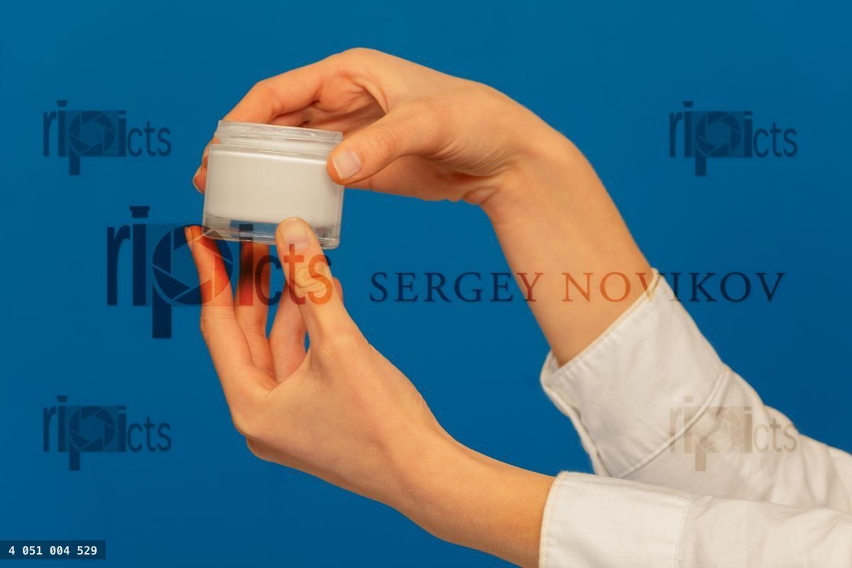 Woman's hands holding cosmetic cream container on blue